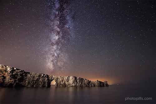 chùm ánh sáng của dải Ngân Hà theo hướng dọc trên cầu đá tự nhiên ở Menorca, Tây Ban Nha.